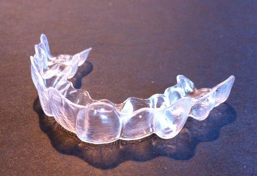 A transparent removable clear-aligner tray on a dark surface.
